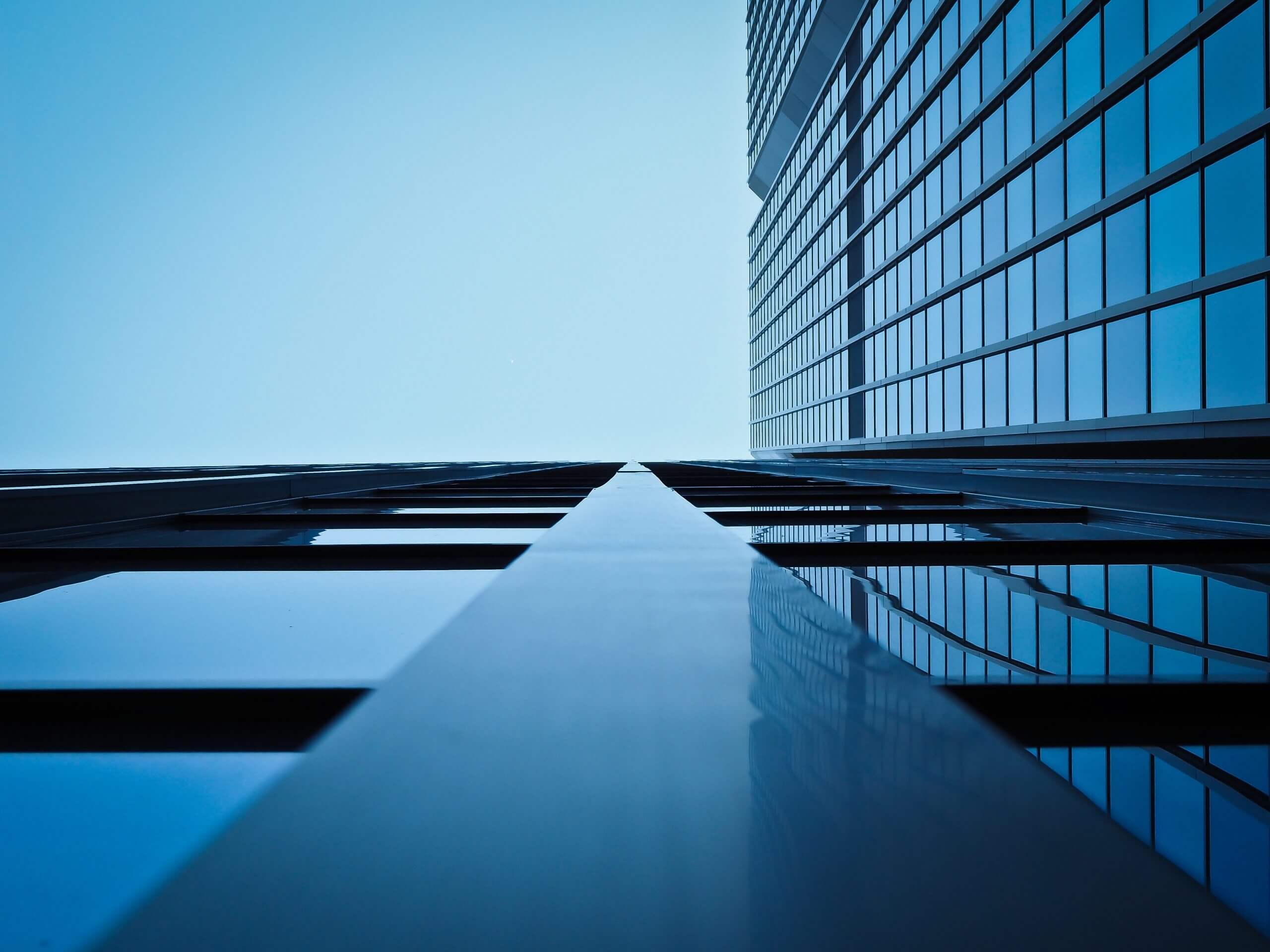 Looking up at a modern glass skyscraper with clear blue sky.