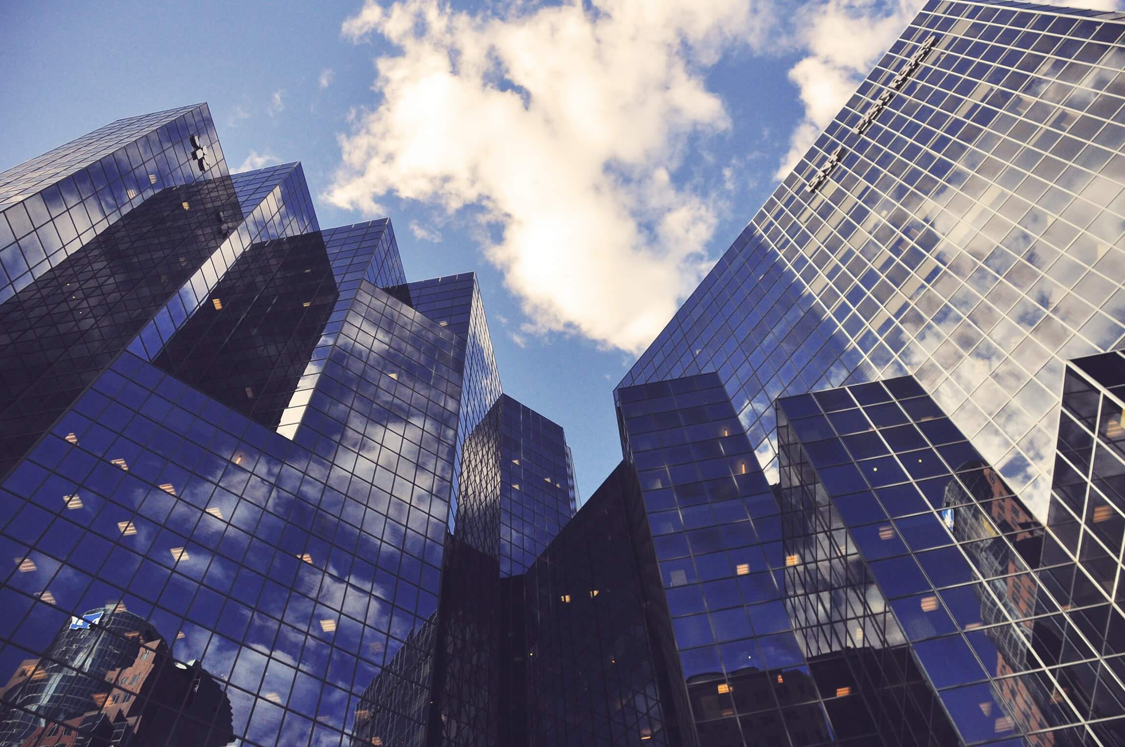 Modern glass skyscrapers reflecting the blue sky and clouds.