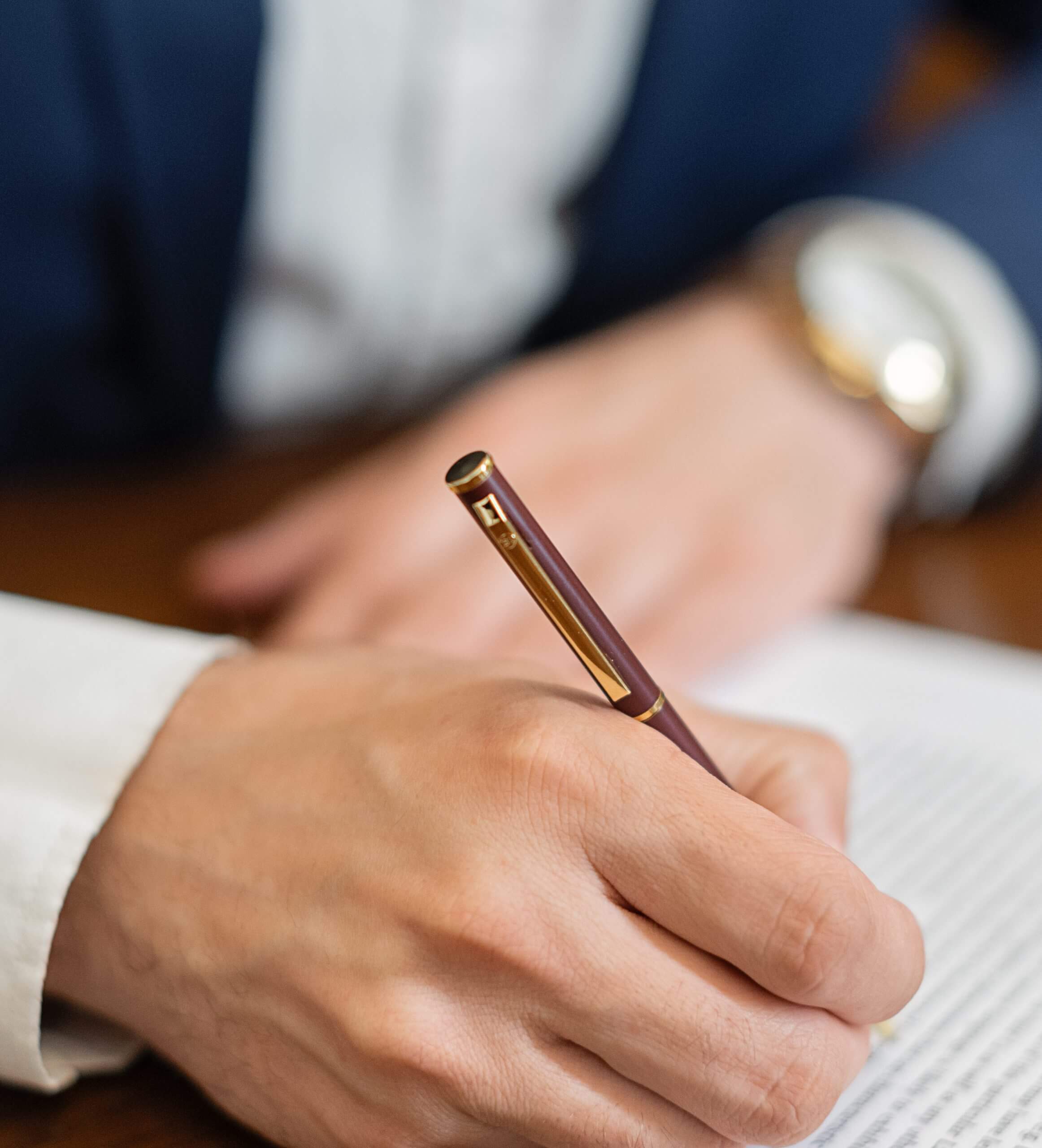 Person writing with a pen on paper, dressed in formal attire.